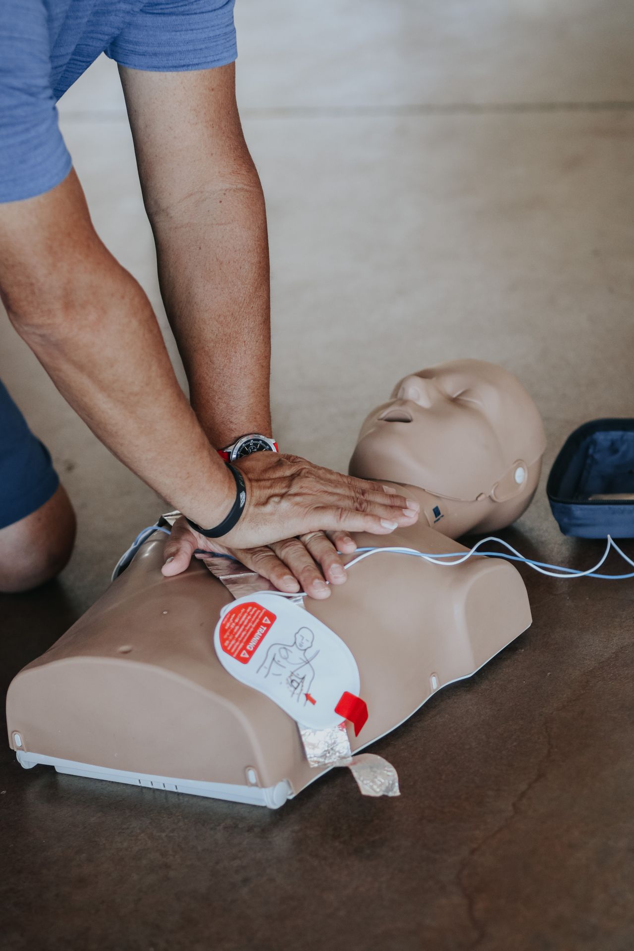 Hands performing CPR on a training manikin fitted with AED defibrillator pads